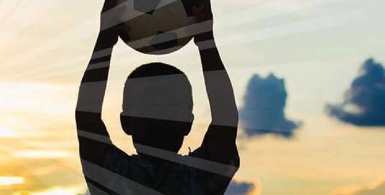 Child holding a soccer ball over his head with the suns rays coming from behind him