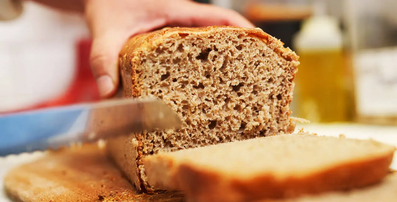 Someone cutting fresh bread into slices on a cutting board