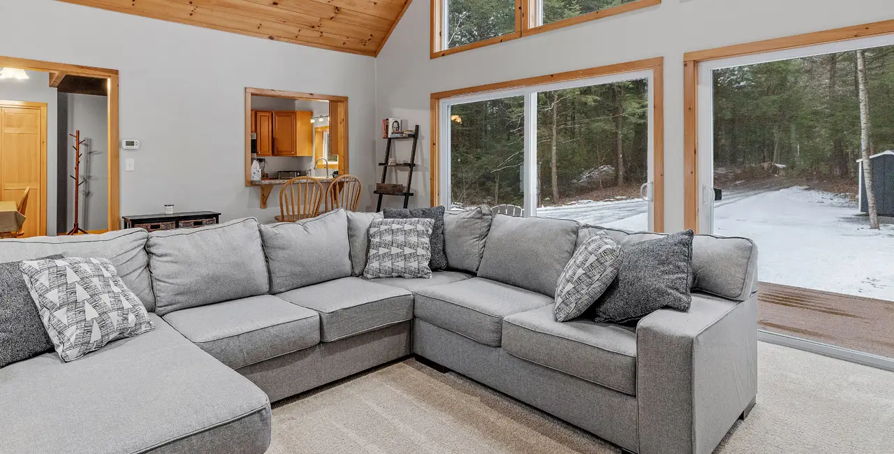 A grey sectional in front nice large windows showing the winter nature.